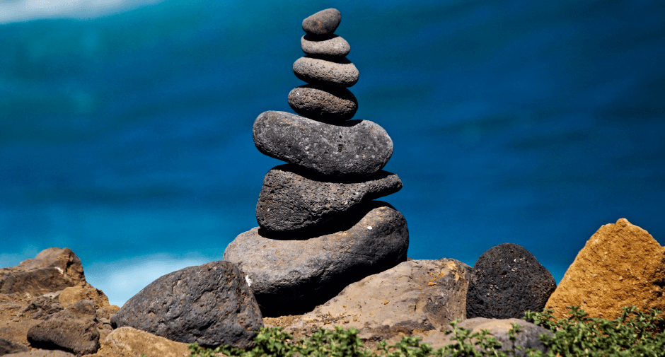 Stabilität der Persönlichkeit, dargestellt mittels eines Turms aus Steinen unterschiedlicher Größe. Im Hintergrund ist das Meer.